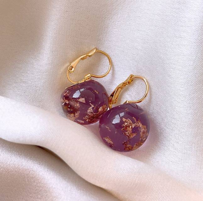 Purple earrings with gold hooks on a beige fabric background
