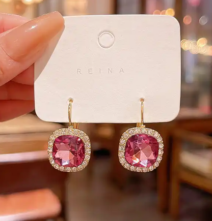 Pink gemstone earrings on a REINA branded card held by a hand.